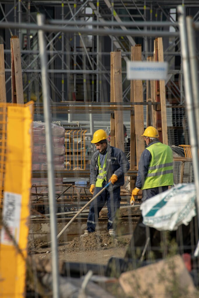 Two construction workers in safety gear collaborate efficiently in a busy construction site, emphasizing teamwork and hard work.