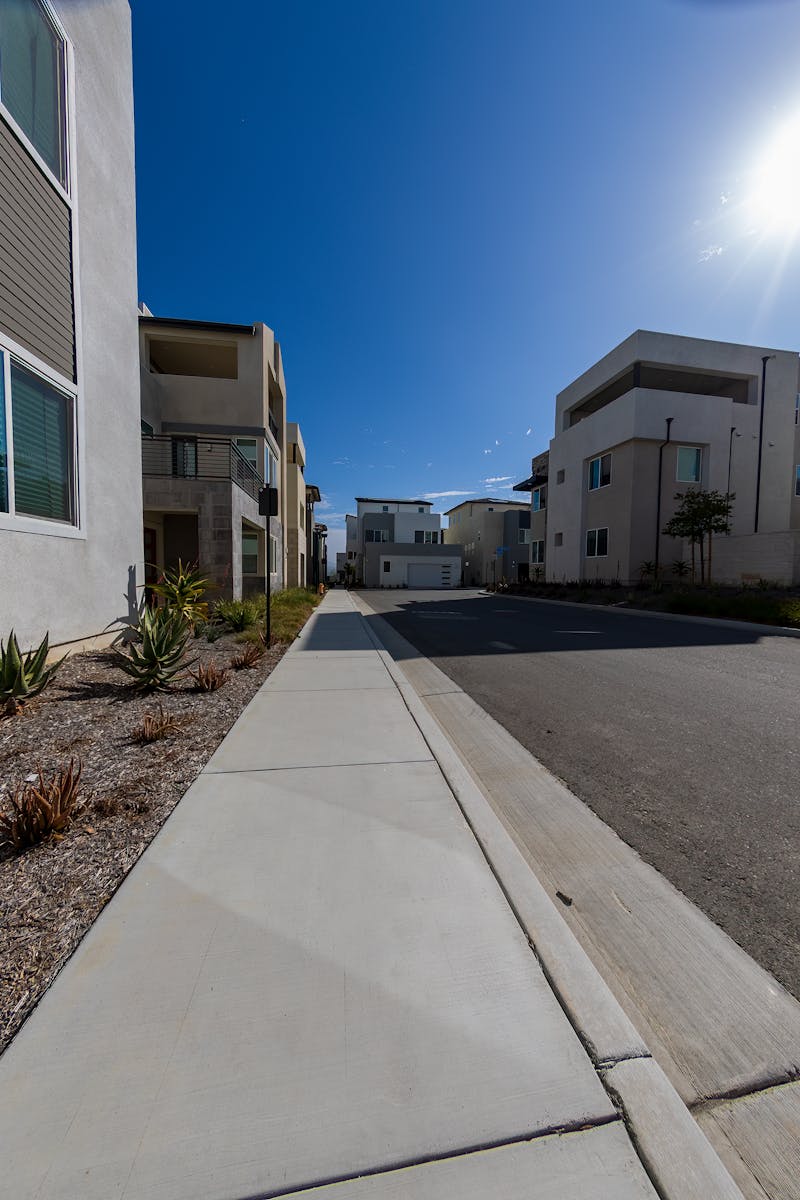 Wide-angle view of a sunny suburban street with modern homes and a clear blue sky, capturing peaceful residential living.