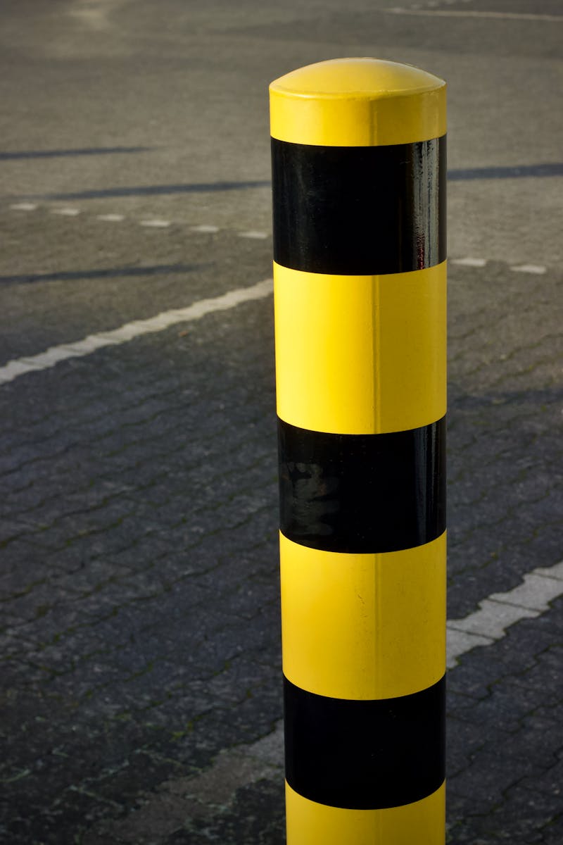 A yellow and black striped traffic bollard stands on a paved road surface.